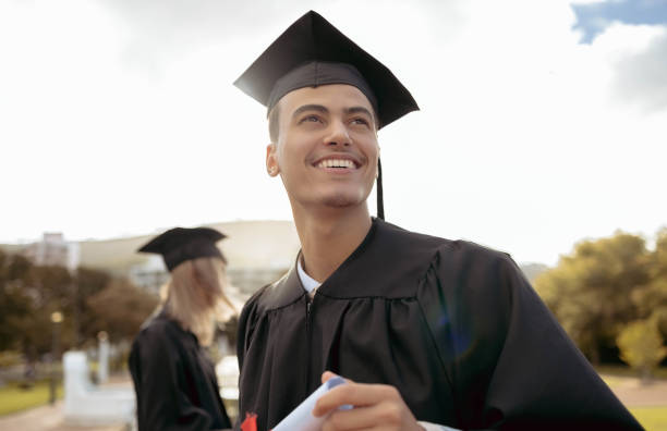 A smiling graduate in cap and gown holding a diploma